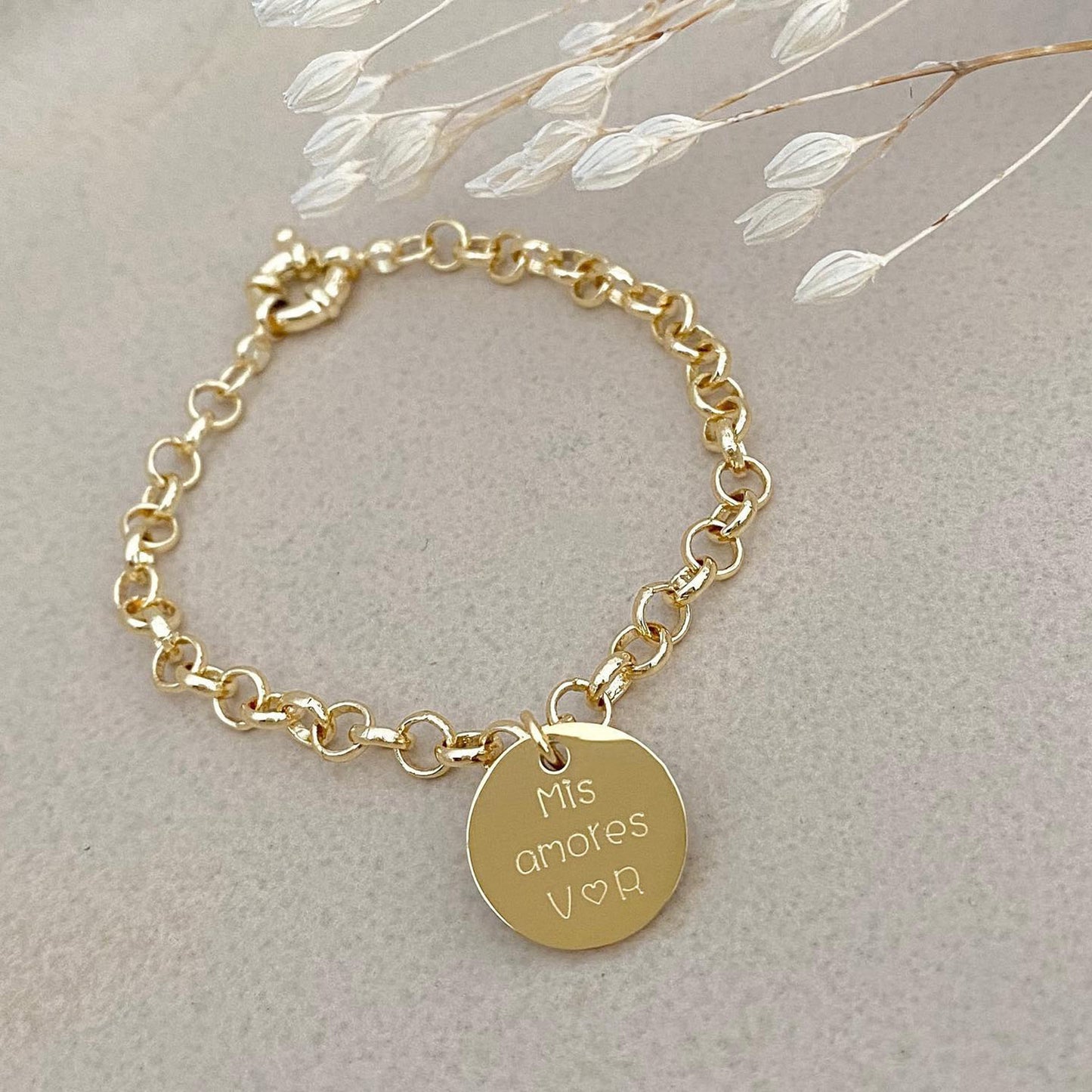 Pulsera formada por una cadena de color dorado con un dije de color dorado que tiene una frase grabada en su superficie.