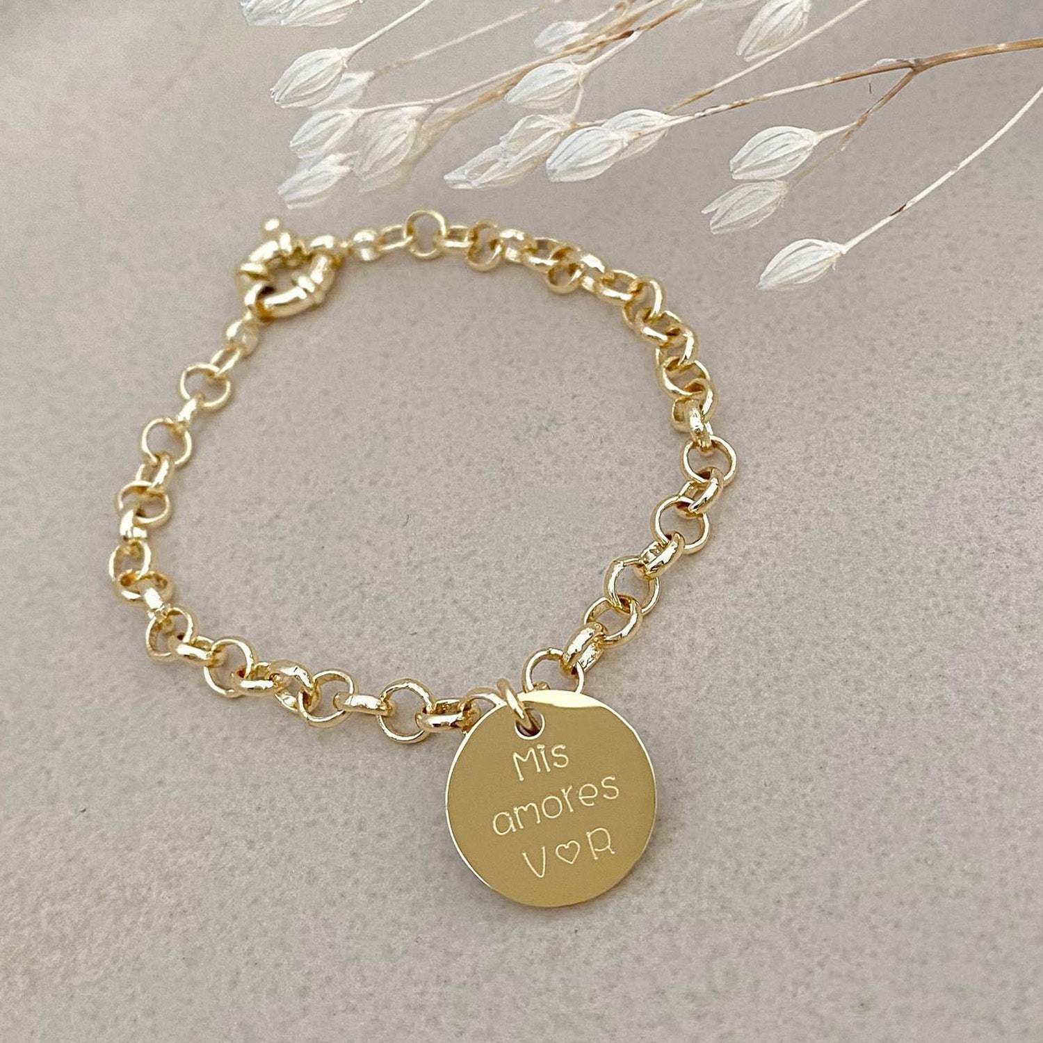 Pulsera formada por una cadena de color dorado con un dije de color dorado que tiene una frase grabada en su superficie.