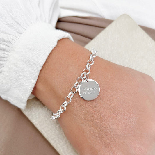 Pulsera formada por una cadena de color plateado con un dije de color plateado que tiene una frase grabada en su superficie.