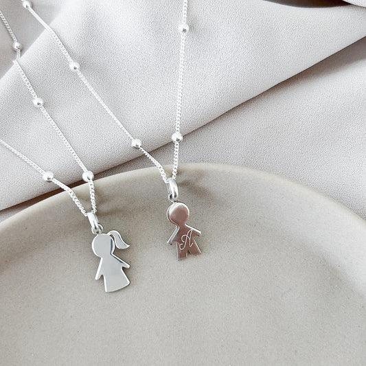 Dos collares, cada uno conformado por una cadena de color plateado. Uno de los collares tiene un dije de  con la forma de la silueta de un niño de color plateado con una inicial grabada en su superficie. El otro collar tiene un dije con la forma de la silueta de una niña de color plateado.