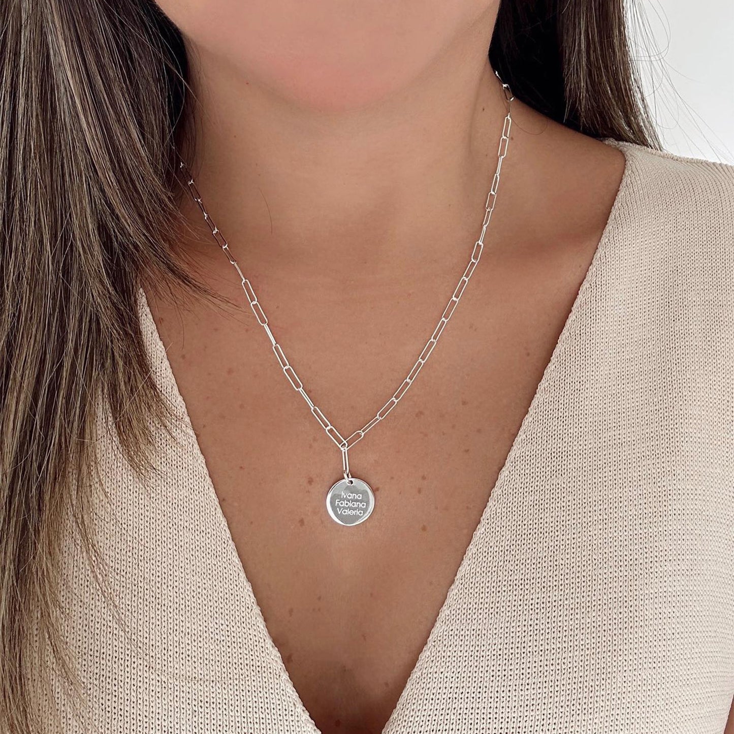 Mujer usando un collar de cadena de color plateado con un dije plateado que tiene grabado un nombre.
