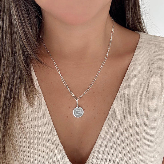 Mujer usando un collar de cadena de color plateado con un dije plateado que tiene grabado un nombre.