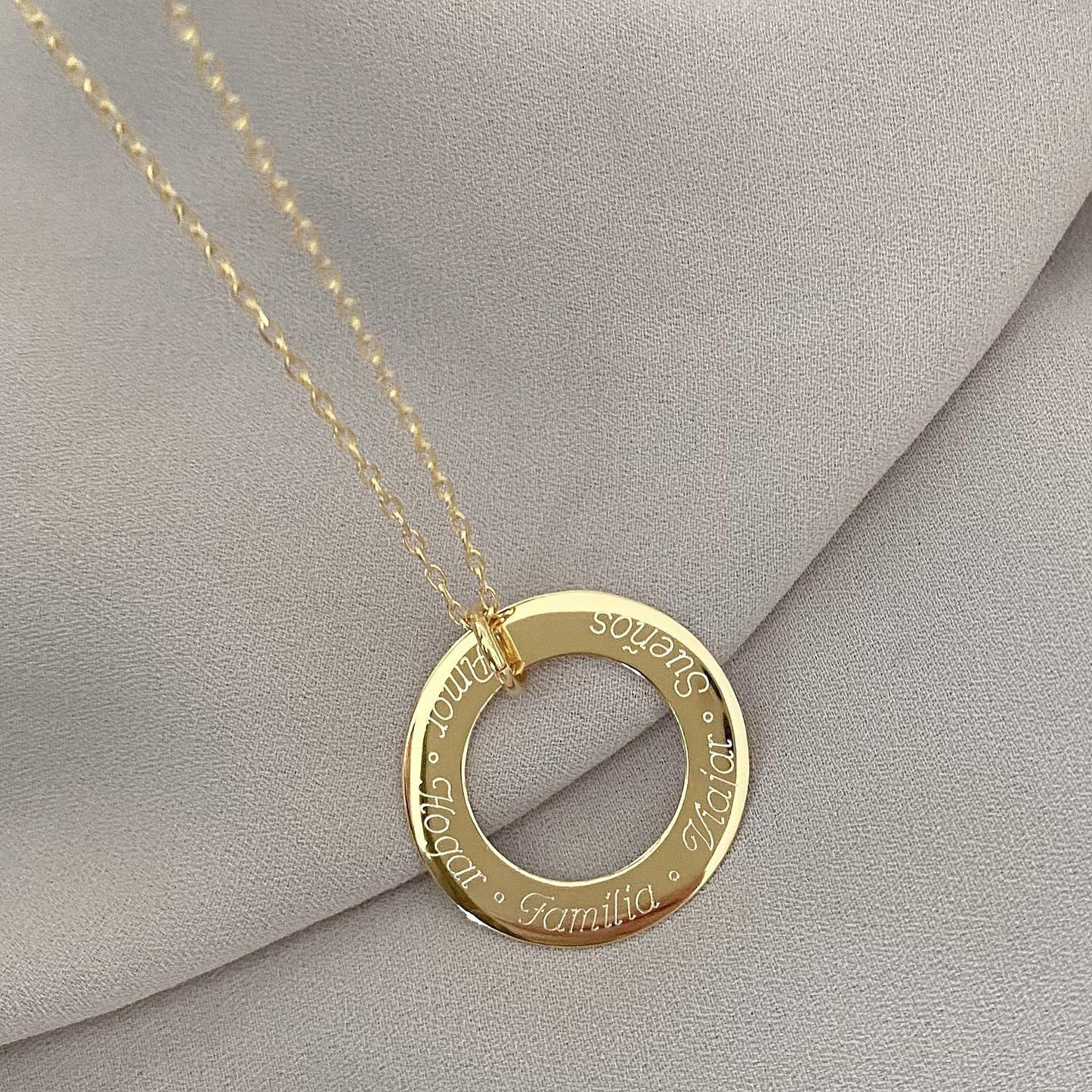 Pulsera formada por una cadena de color dorado con un dije redondo de color dorado que tiene una frase grabada en su superficie.