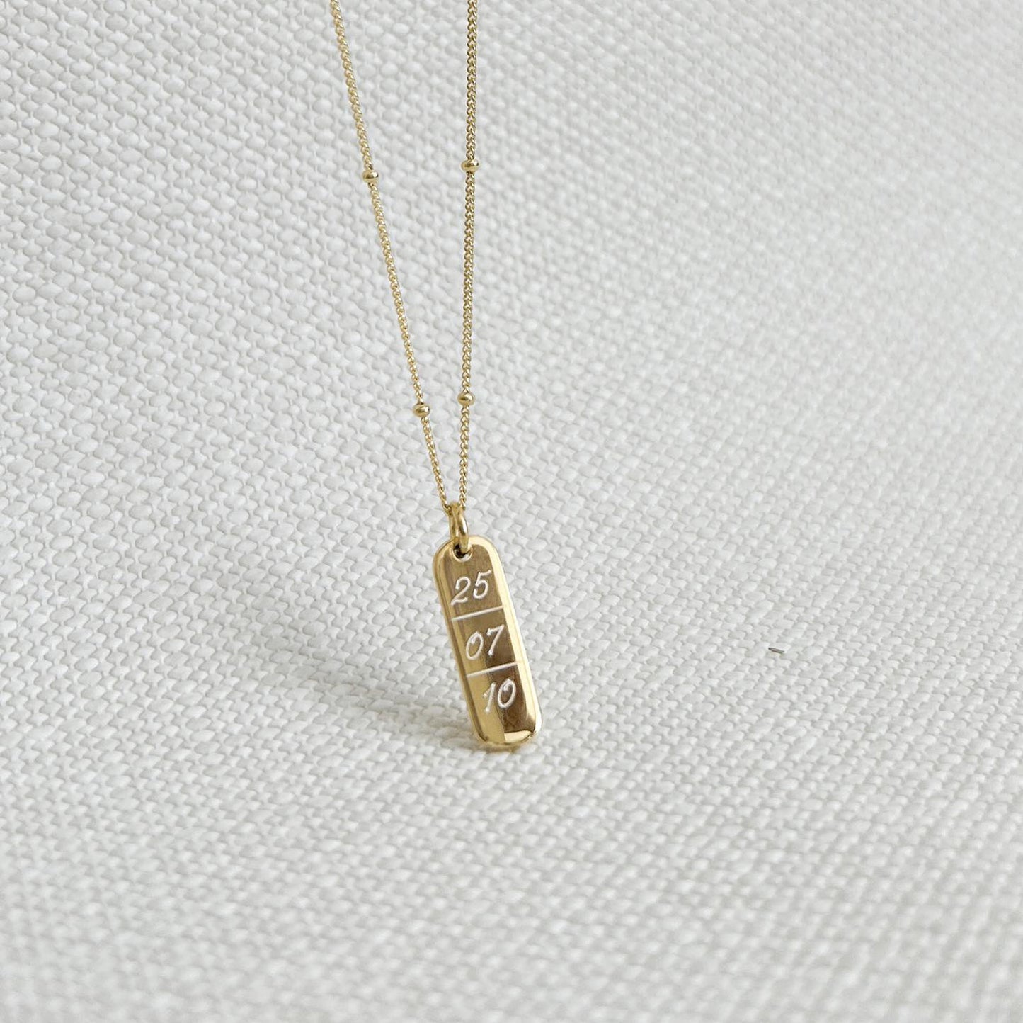 Collar formado por una cadena de color dorado con un dije de color dorado que tiene una fecha  grabada en su superficie.