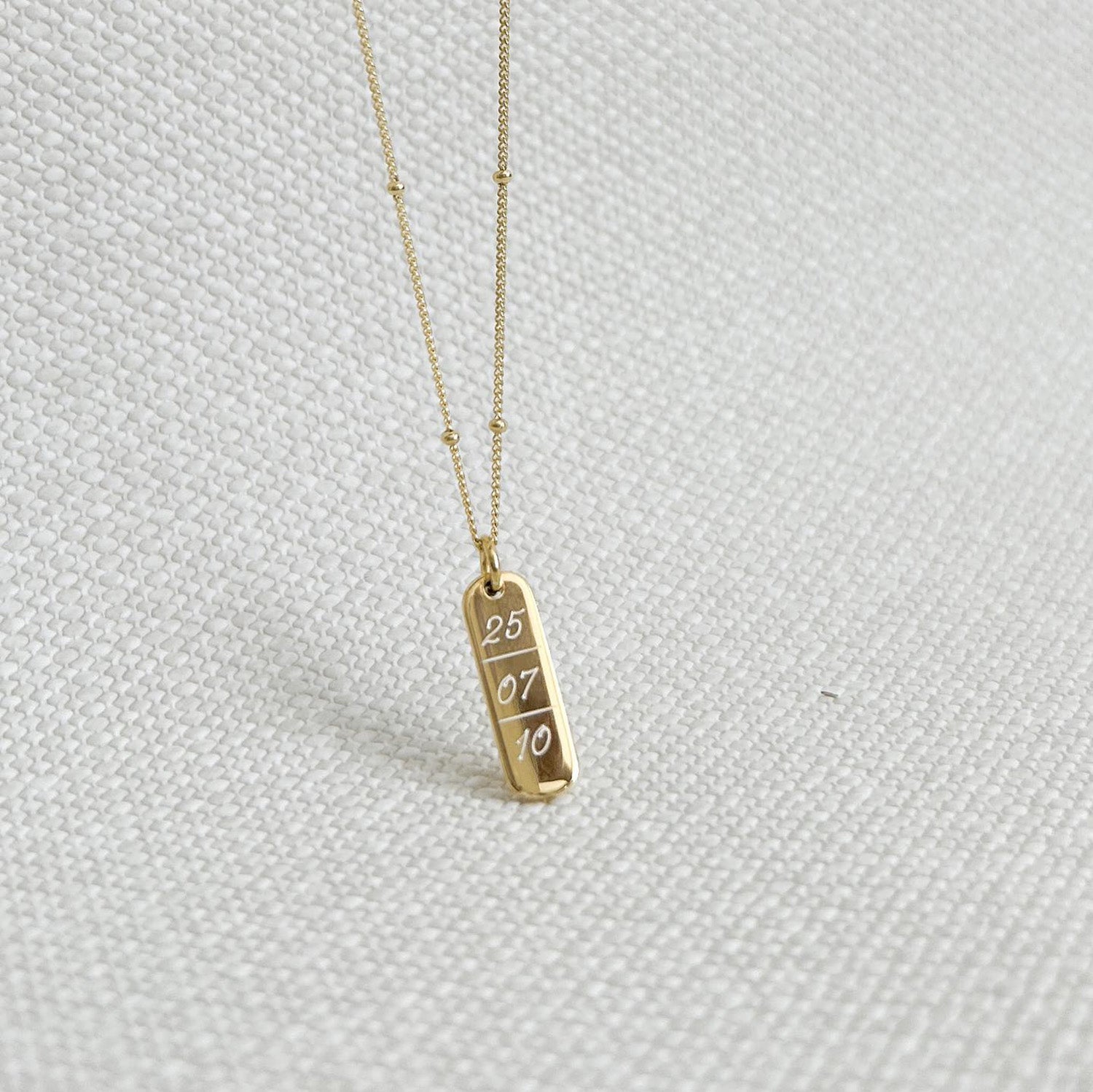 Collar formado por una cadena de color dorado con un dije de color dorado que tiene una fecha  grabada en su superficie.