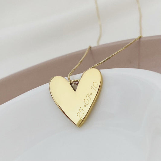 Collar formada por una cadena de color dorado con un dije en forma de corazón de color dorado que tiene una fecha grabada en su superficie.