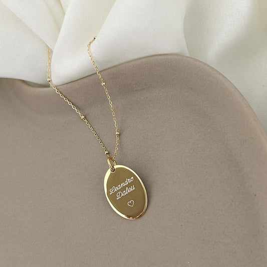 Cadena de color dorado con un dije dorado que tiene un nombre y un corazón inscritos en él.