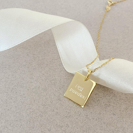 Collar formado por una cadena de color dorado con un dije de color dorado que tiene una frase grabada en su superficie.