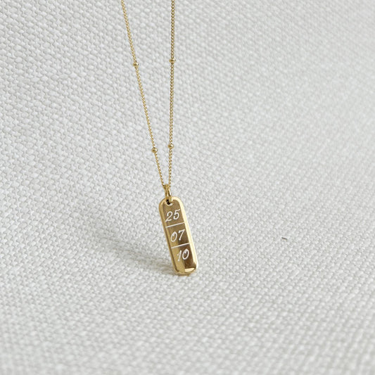 Collar formado por una cadena de color dorado con un dije de color dorado que tiene una fecha  grabada en su superficie.